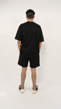 Man seen from behind wearing the Fear of God Essentials FW24 Black Yellow Summer Set with black oversized t-shirt, matching shorts, and black and white sneakers, showcasing a clean and minimalist summer look.