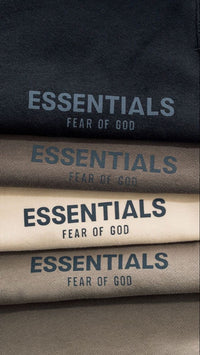 Close-up of four stacked Fear of God Essentials NBA Black White Summer Set sweatshirts in black, gray, cream, and taupe colors, showcasing the ESSENTIALS logo print, the real deal exclusive clothing.