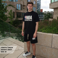 Man wearing Fear of God Essentials NBA Black White Summer Set with NBA logo t-shirt and matching shorts, styled with sneakers in an urban outdoor setting, showcasing exclusive European streetwear.