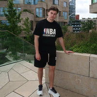 Young man wearing Fear of God Essentials NBA Black White Summer Set with black NBA Essentials t-shirt and matching shorts, styled with exclusive sneakers in an urban outdoor setting, embodying The real deal.