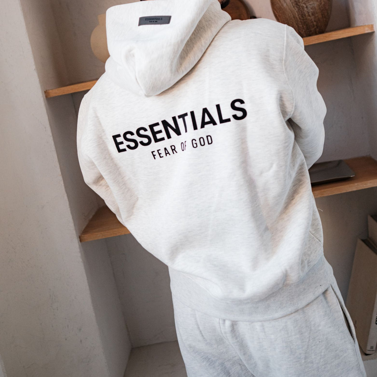 Fear of God Essentials Light Oatmeal Hoodie, achteraanzicht hangend met groot geborduurd logo zichtbaar