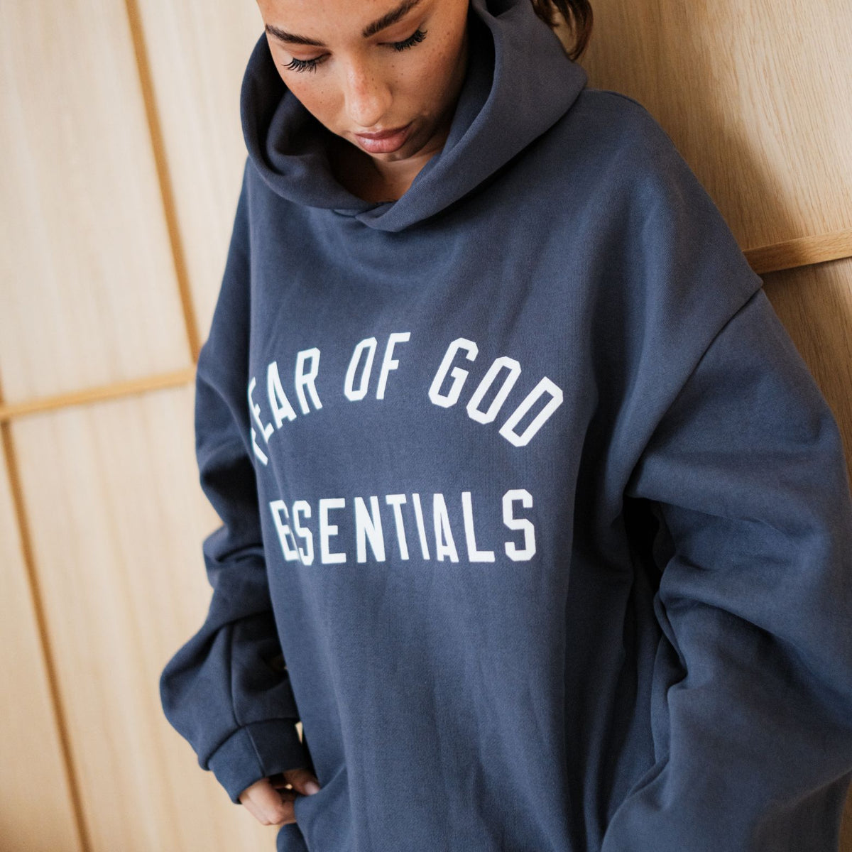 Fear of God Essentials FW24 Marine Hoodie, vooraanzicht omlaag kijkend met wit tekstlogo op marineblauw