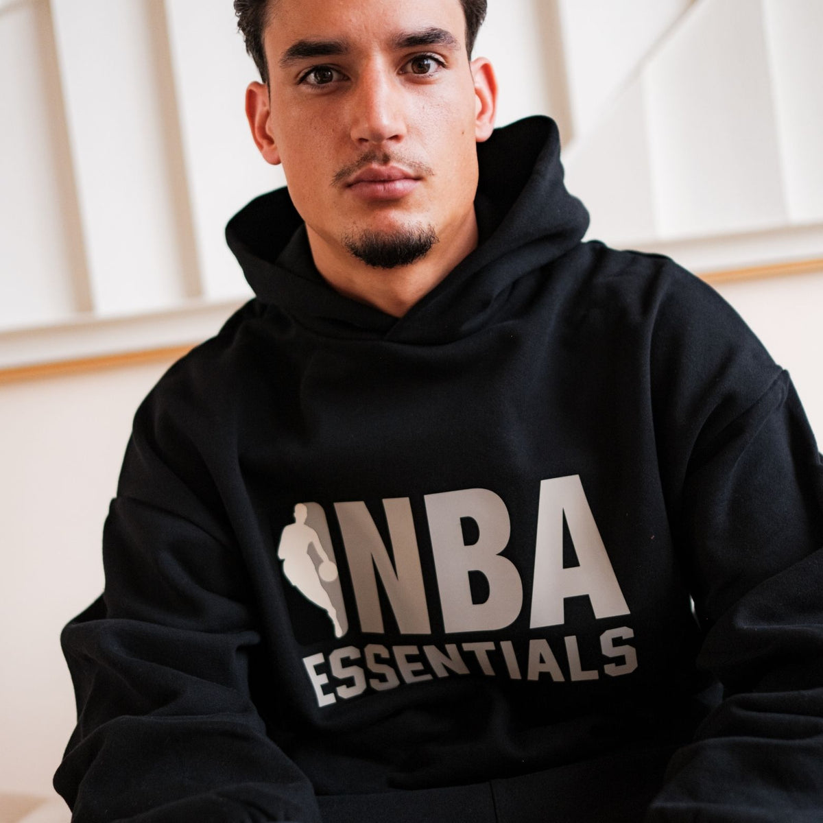 Fear of God Essentials NBA Black Grey Hoodie, detailfoto vooraanzicht van hoodie met wit NBA-logo en grijze tekstaccenten
