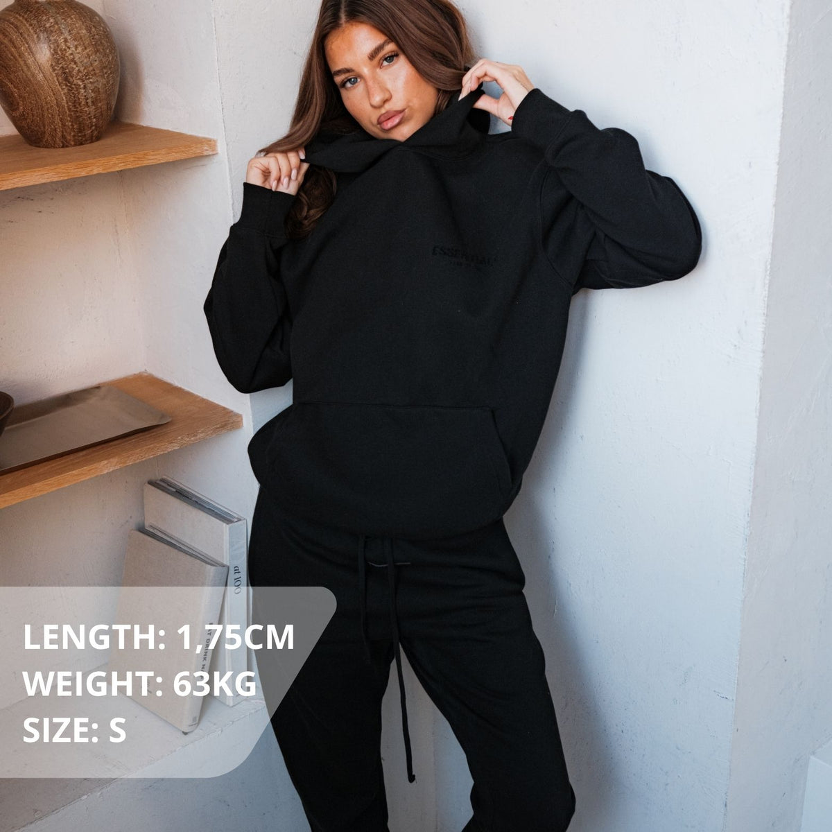 Fear of God Essentials Stretch Limo Hoodie, gedragen met volledige zwarte outfit en trekkoord zichtbaar